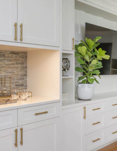 A modern kitchen with white cabinetry, gold handles, and a stone backsplash with a potted plant on the countertop.