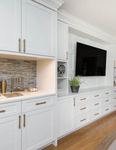 A modern home office with built-in white cabinets, a stone accent wall, and a mounted television.