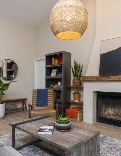 Cozy living room interior with a fireplace, wicker pendant lamp, and modern furnishings.