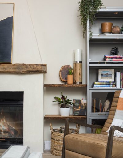 Cozy living room corner with fireplace, wooden mantel shelves, and a comfortable brown armchair.