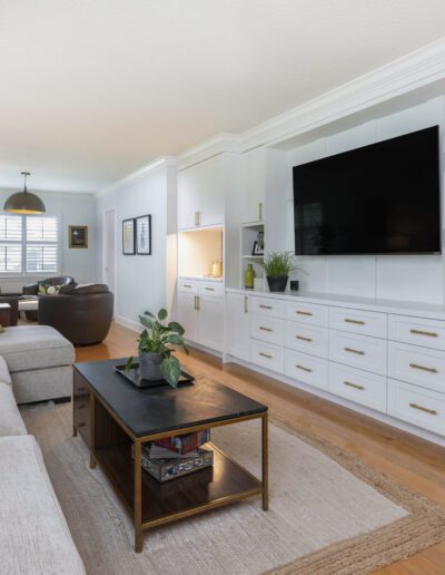 Bright and modern living room with built-in white cabinets and a large screen tv.