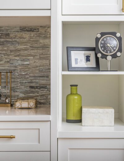 Elegant home office shelves styled with decorative items, including a plant, clock, and photo frame, against a backdrop of a stone tile wall.