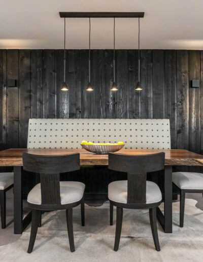 Modern dining area with black accent wall and hanging pendant lights over a wooden table with a tufted bench and chairs.