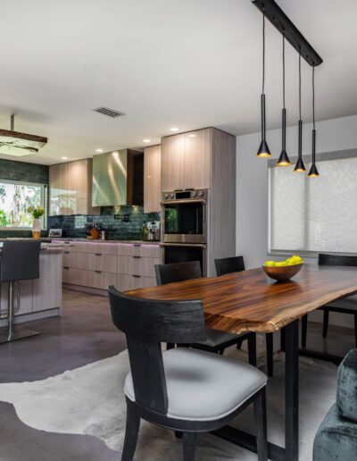 Modern kitchen and dining area with sleek design, featuring a wood table, pendant lights, and stainless steel appliances.