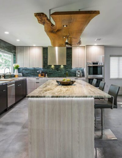 Modern kitchen with a large central island, stainless steel appliances, dark cabinetry, and a distinctive wooden range hood.