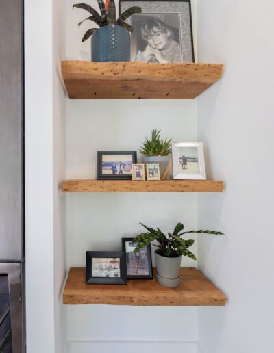 Three wooden shelves on a wall displaying framed photographs and potted plants.