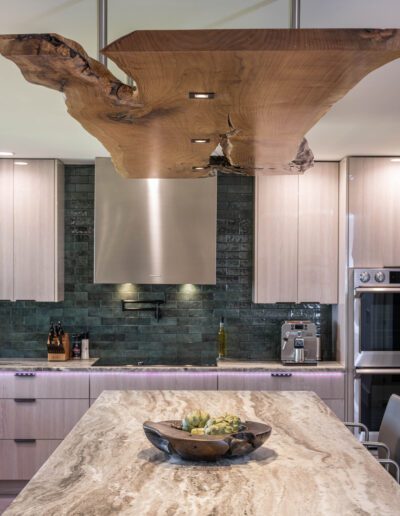 Modern kitchen with a large wooden sculptural element above the island, stone countertops, and a blue tile backsplash.