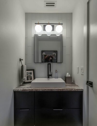 Modern bathroom with a dark vanity, vessel sink, and a mirror flanked by globe lights.