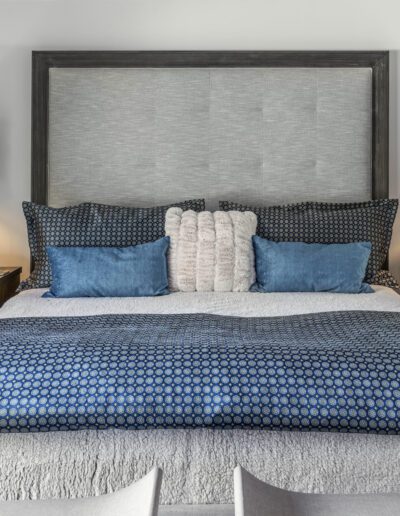 A neatly made bed with blue and gray bedding flanked by hanging pendant lights and a nightstand with a lamp.