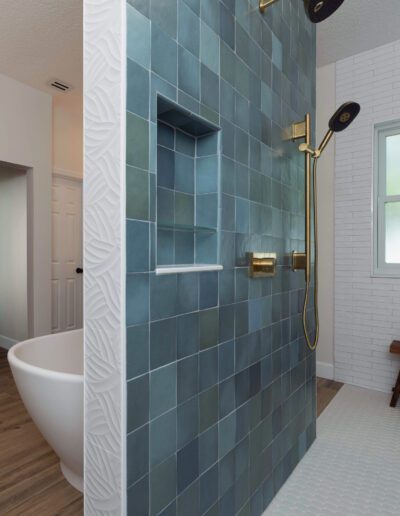 Modern bathroom with blue tile shower, white freestanding tub, and wooden floor.