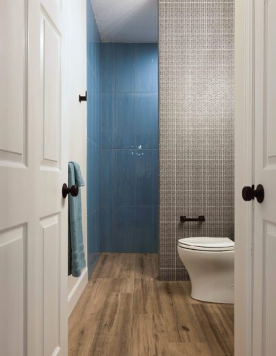 Modern bathroom with contrasting blue and beige tiled walls, wooden floor, and white fixtures.