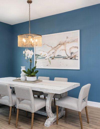 Modern dining room with blue walls, a white table, gray chairs, and a large wall art piece.