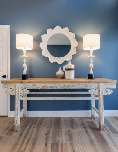 An elegant, vintage wooden console table with matching lamps and decorative mirror against a blue wall.