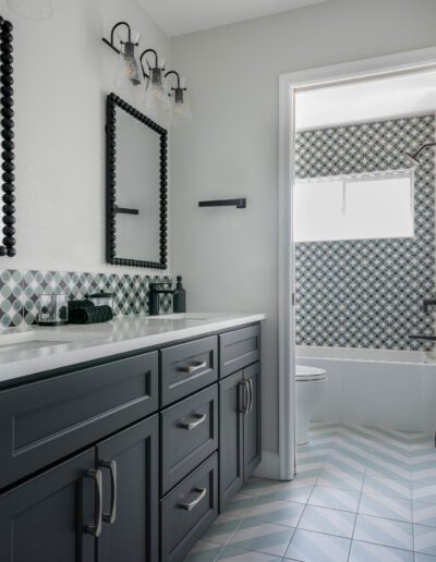 Modern bathroom interior with geometric patterned tile and sleek dark gray cabinetry.