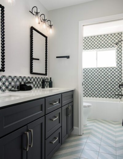 Modern bathroom with geometric tile design, black cabinetry, and herringbone floor pattern.