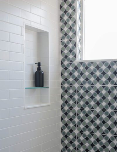 Modern bathroom corner with white subway tiles and a patterned shower wall, featuring a built-in niche with a black soap dispenser.