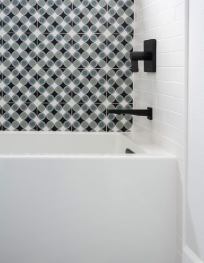 Modern bathroom with geometric tiled wall and white bathtub.