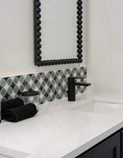 Modern bathroom vanity with a black faucet, white countertop, and a decorative tiled backsplash.