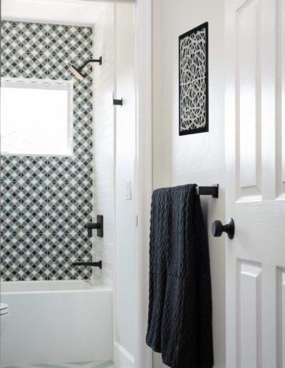 A modern bathroom with geometric patterned tiles and a dark towel hanging on a black towel bar.