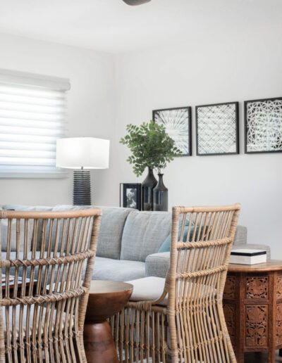 Modern living room interior with rattan chairs, a gray sofa, decorative wall art, and plant accent.