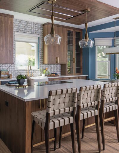 Modern kitchen interior with wooden cabinets, patterned backsplash, and a central island with bar stools.