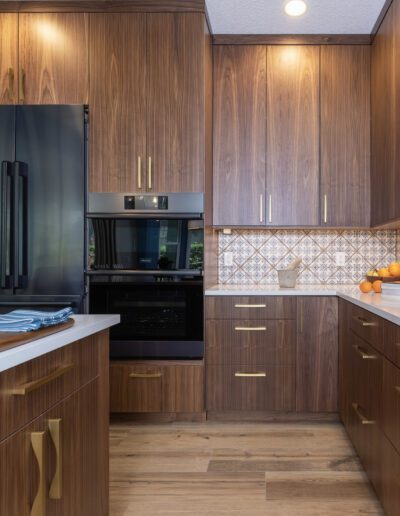 Modern kitchen interior with wooden cabinetry, stainless steel appliances, patterned backsplash, and hardwood flooring.