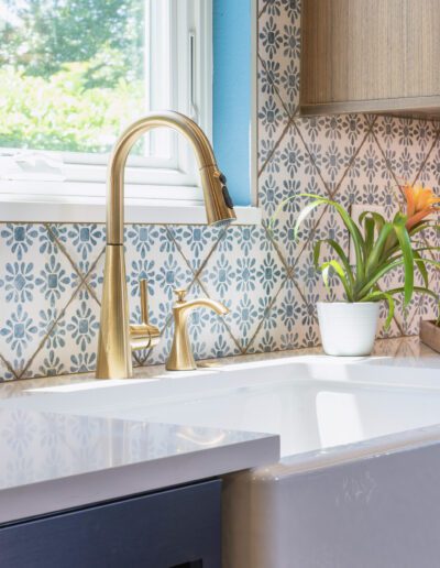 Modern kitchen sink with a gold faucet, set against a patterned tile backsplash, near a window with a garden view.