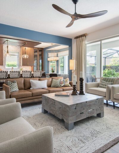 A modern, spacious living room with an open kitchen design, featuring a combination of neutral tones and a touch of blue, complemented by natural light and indoor greenery.