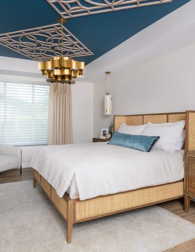 A stylish modern bedroom featuring a bed with a wooden headboard, matching nightstands, elegant gold and blue ceiling design, and ample natural light.