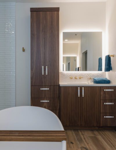 Modern bathroom interior with wooden cabinets, white textured walls, and built-in bathtub.