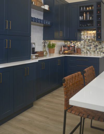 Modern kitchen with navy blue cabinetry, brass hardware, and a patterned backsplash, featuring a white countertop and bar seating with woven chairs.