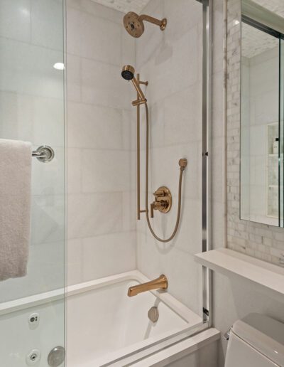 A modern bathroom featuring a glass-enclosed shower and bathtub combination with gold fixtures.