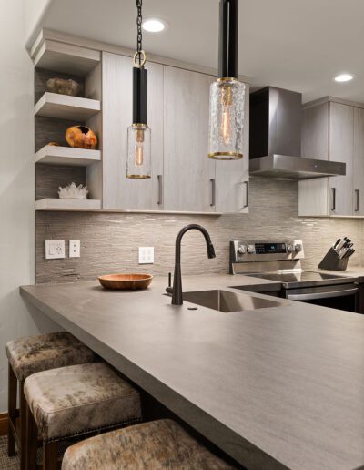 Modern kitchen interior with a clean design, featuring gray countertops, wooden cabinets, and pendant lighting.