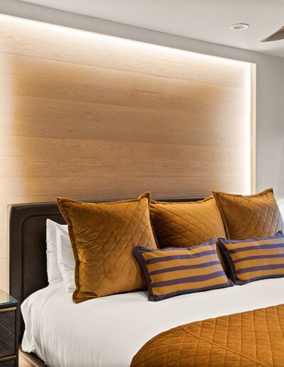 Modern bedroom interior with a large bed, gold and brown pillows, hanging pendant lights, and a view of the balcony.