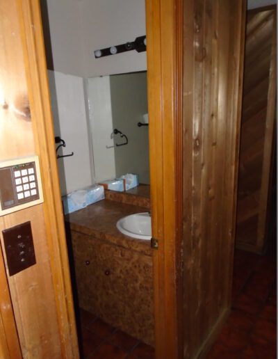 Interior view of a bathroom with wooden doors open, showcasing a sink and mirror with dim lighting.