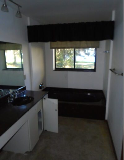 Dimly lit kitchen with black countertops, a double sink, and a window with a valance curtain.